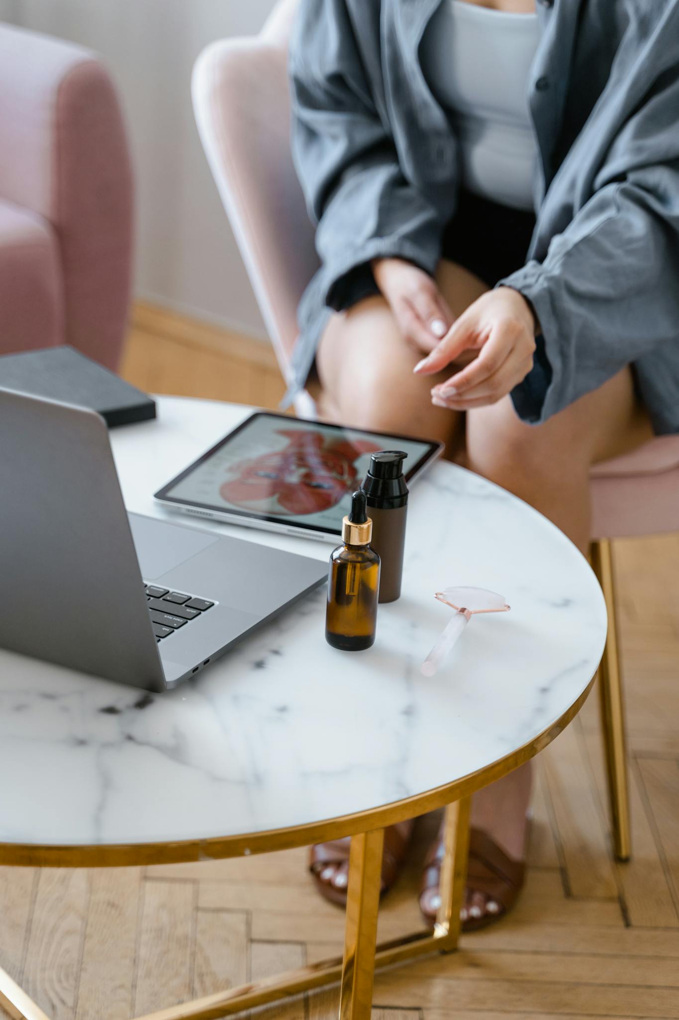 Woman working remotely, surrounded by skincare products on a round marble table.